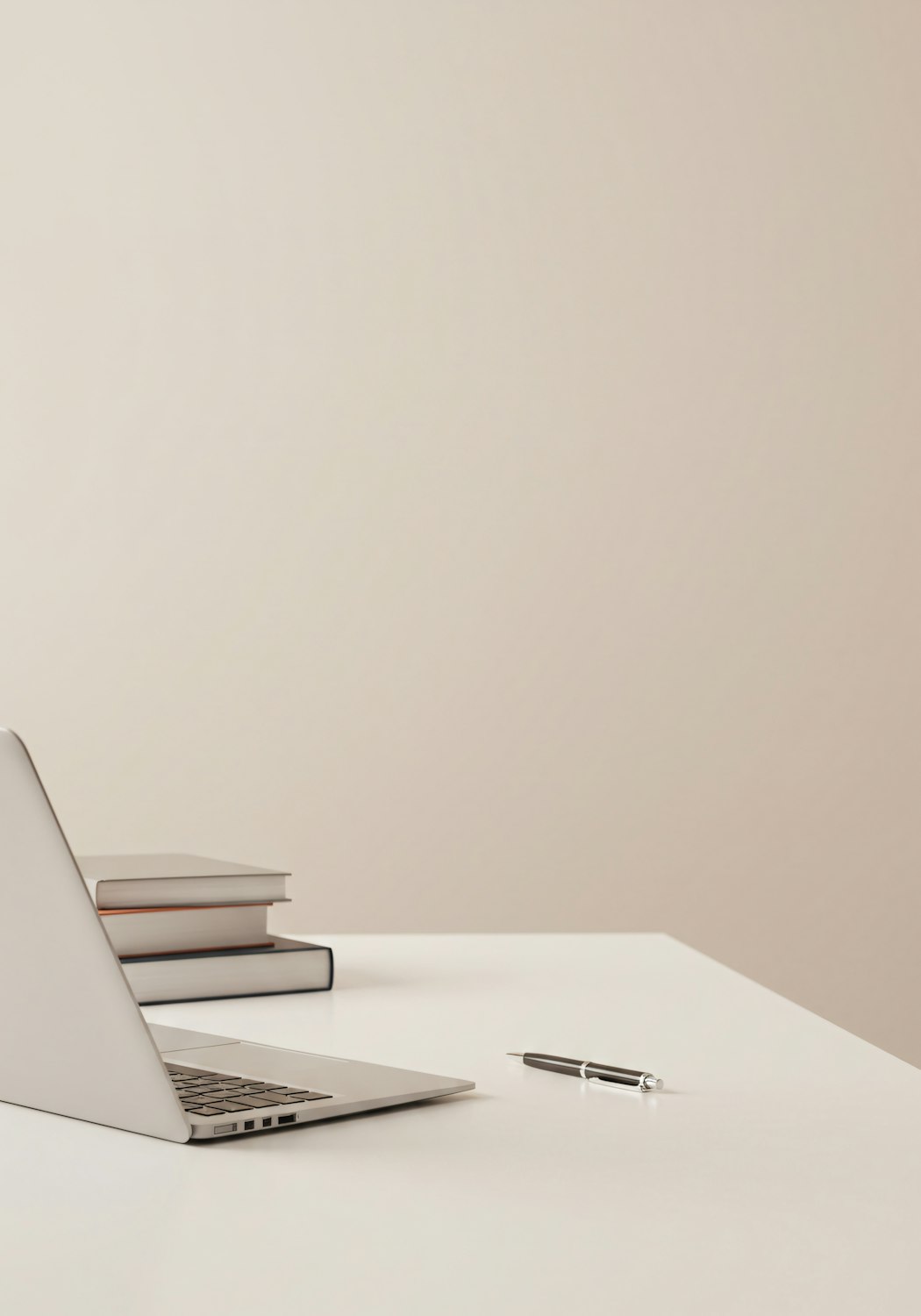 Minimal workspace with a laptop, books and a pen on a white desk
